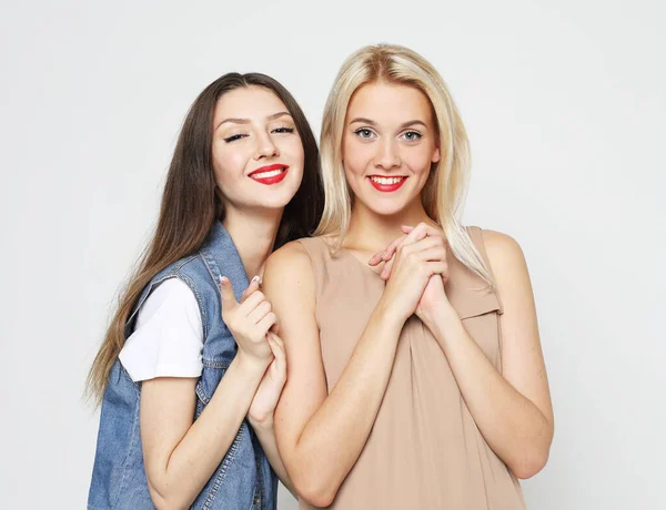 Close-up portret van twee jonge vrouwen die casual dragen. Meisjes glimlachen, veel plezier tegen grijze achtergrond. — Stockfoto