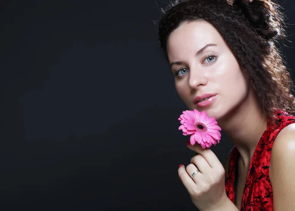 Joven hermosa mujer vistiendo vestido rojo sosteniendo flor gerber rosa — Foto de Stock