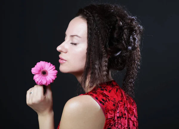 Joven hermosa mujer vistiendo vestido rojo sosteniendo flor gerber rosa —  Fotos de Stock