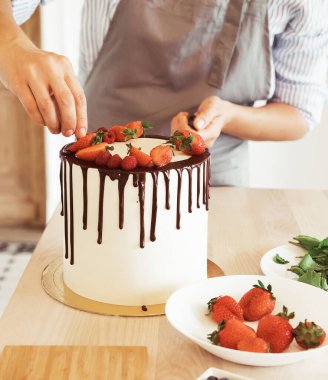 Genç bayan mutfakta çikolatalı ve çilekli bisküvi keki yapıyor..