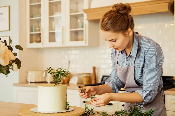 Young woman pastry chef in the kitchen decorating cake with flowers and berries. — Stock Photo, Image