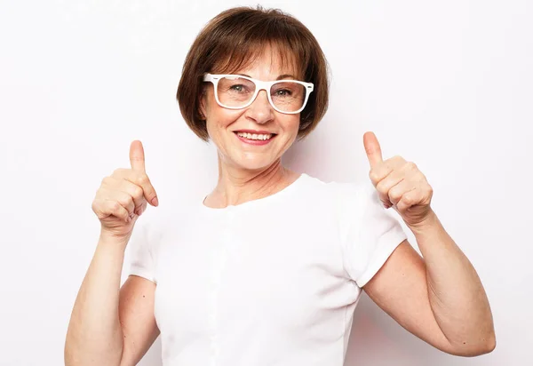 Portrét veselé stařeny v bílém tričku a brýlích ukazující palce nahoru — Stock fotografie