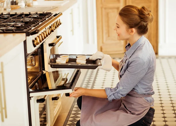 A young woman bakes muffins, takes them out of the oven, puts the pastries in the oven. — Stock Photo, Image