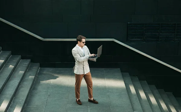 Young handsome businessman spending time outdoors at the city, using laptop computer on stairs — Stock Photo, Image