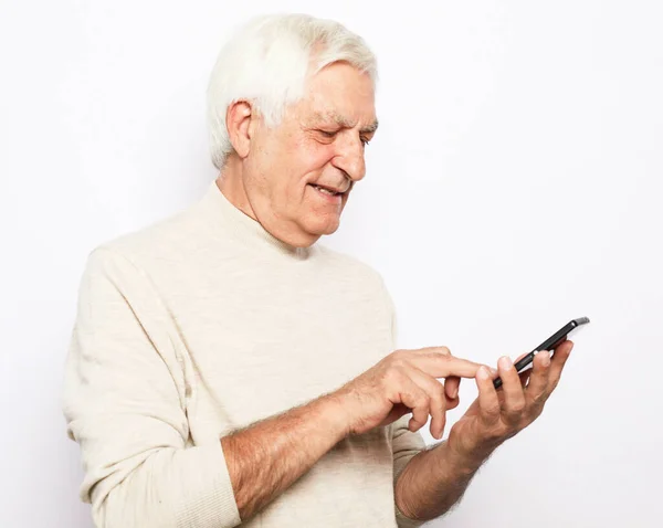 Senior man i casual outfit glatt leende och med modern smartphone — Stockfoto