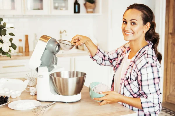 Young woman uses mixer and whips cream for cake, stands in modern kitchen — Stock Photo, Image