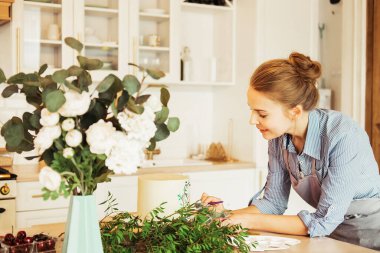 Genç kadın pasta şefi mutfakta. Pastayı çiçekler ve böğürtlenlerle süslüyor..