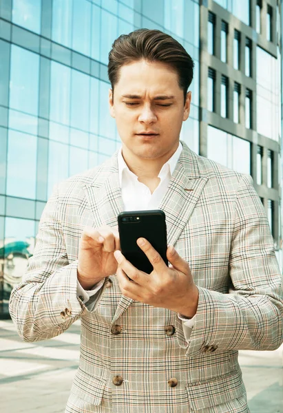 Empresario que utiliza mensajes de texto de aplicaciones para teléfonos móviles fuera de la oficina en la ciudad urbana con edificios de rascacielos en el fondo. —  Fotos de Stock