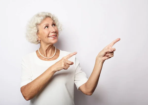 Usmívající se starší žena s krátkými vlasy izolované na bílém pozadí studio ukazuje prstem na prázdné kopie prostoru stranou — Stock fotografie