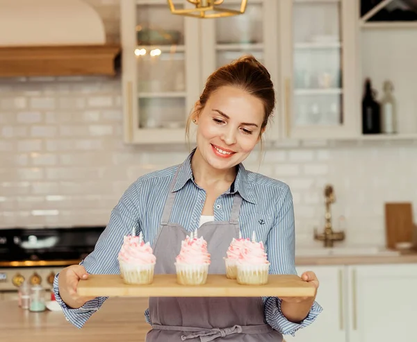 Egy fiatal pék nő sütit tart. Boldog, mosolygós és vidám.. — Stock Fotó