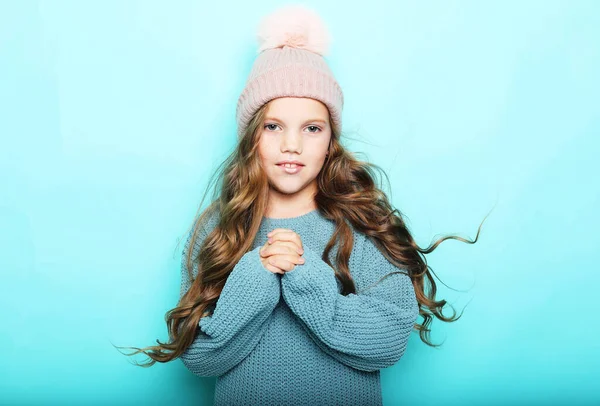 Πορτρέτο θετικού χαμογελαστού παιδιού με ξανθά κυματιστά μαλλιά και χειμερινό καπέλο. Ευτυχισμένο όμορφο όμορφο κορίτσι κοίτα την κάμερα και χαμογέλα. — Φωτογραφία Αρχείου