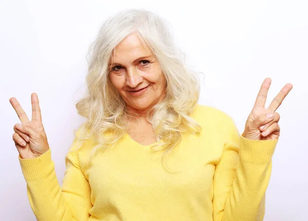 Buen humor feliz sonriente mujer anciana positiva con el pelo blanco, el uso de suéter amarillo muestran v-signo — Foto de Stock