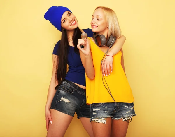 Две юные подруги носят случайные стоя вместе и веселятся на жёлтом фоне. — стоковое фото
