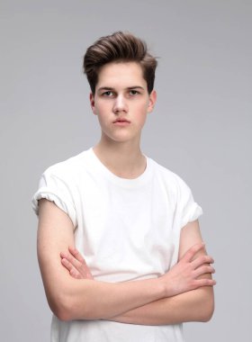 Gri arka planda kollarını çapraz yapmış yüksek model bir adam. Yakından bakınca yakışıklı biri. Şık saç kesimi, saç şekli..