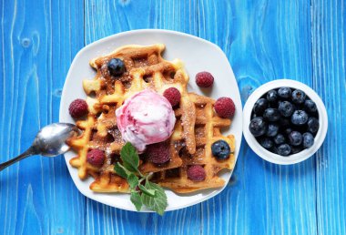 Taze böğürtlenli Belçika waffle 'ları ve mavi ahşap arka planda dondurma.