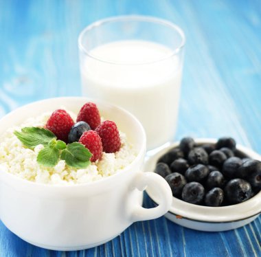 Mavi ahşap arka planda taze böğürtlen ve sütle süzme peynir. Kapat..