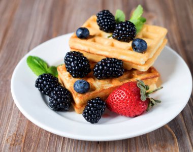 Ev yapımı Belçika waffleları, ahşap arka planda taze böğürtlenlerle servis edilir.