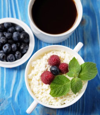 Mavi ahşap arka planda taze böğürtlenli süzme peynir ve kahve. Kapatın. Üst görünüm.