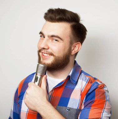 Gri arka planda mikrofonla şarkı söyleyen sakallı yakışıklı bir adam.