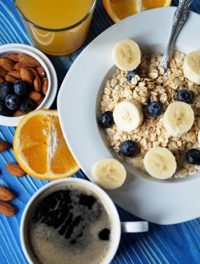 Beyaz tabakta taze böğürtlen ve mavi ahşap arka planda portakal suyu bulunan yulaf ezmesi.