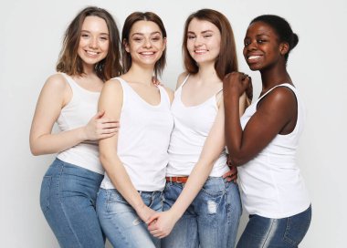 Gri arka planda farklı milletlerden dört genç kadın arkadaş grubu.