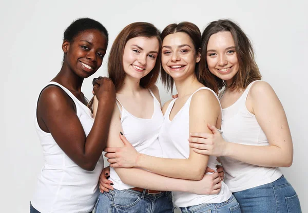 Group of four young women friends of different nationalities over grey background.