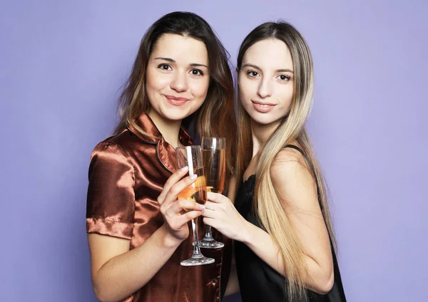 Zwei schöne Frauen im Pyjama trinken Champagner und amüsieren sich über lila Hintergrund — Stockfoto