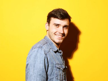 Sarı arka planda kameraya gülümseyen sıradan kıyafetler giyen mutlu esmer bir adam resmi..