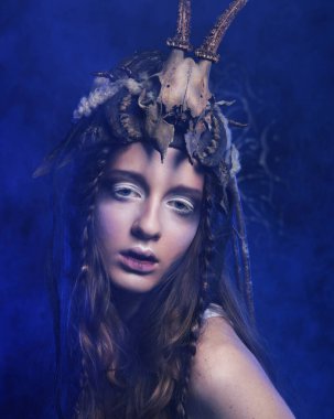 Parlak makyajlı, örgülü ve kafasında kafatası olan genç bir kadın karanlık arka plan partisinde, karnavalda, cadılar bayramında poz veriyor..