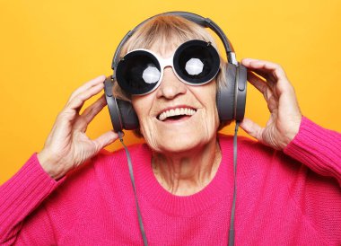 Beyaz arka planda kulaklıkla müzik dinleyen neşeli yaşlı kadın. Yaşam tarzı ve insan kavramı.