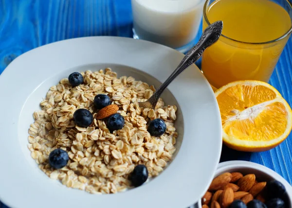 Healthy breakfast, food and diet concept - oatmeal with fresh berries on white plate with orange juice and milk, blue wooden background.