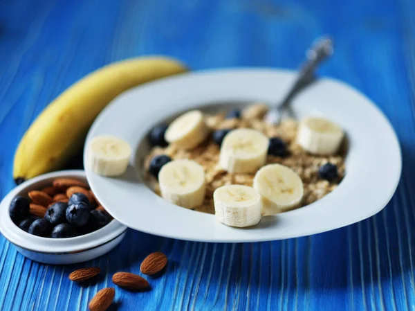 Healthy eating, food and diet concept. Oatmeal with fresh berries with banana and peanuts, white plate, over blue wooden background.