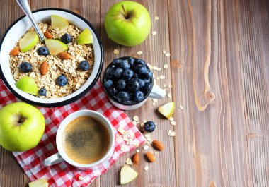 Sağlıklı bir kahvaltı yeni bir güne harika bir başlangıçtır. Tahta bir masada yulaf lapası, kahve, elma, böğürtlen ve fındık. Üst görünüm.