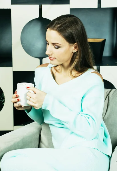 Красива молода жінка тримає чашку кави і сидить на стільці вдома. Стиль життя і концепція людей . — стокове фото