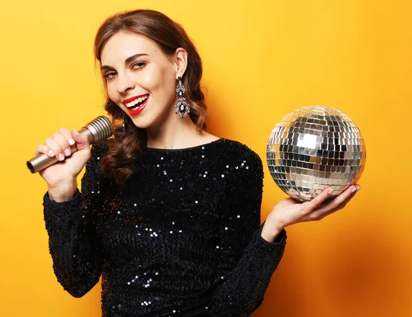 Mujer en vestido de noche sosteniendo micrófono y bola disco . — Foto de Stock