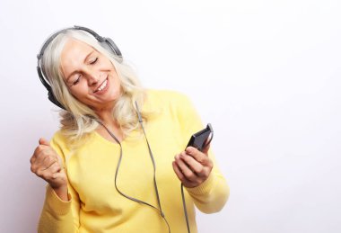 Neşeli yaşlı kadın, beyaz arka planda kulaklıkla müzik dinliyor.