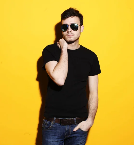 Portrait of a young handsome man dressed casual and wearing sunglasses on yellow background — Stock Photo, Image