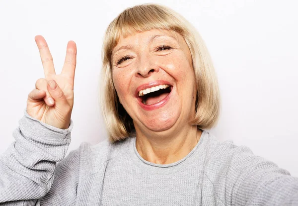 Mujer mayor haciendo selfie con paz cantar y oler. Retrato de la hermosa abuela expresiva usando casual. —  Fotos de Stock