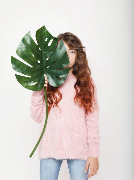 Концепция красоты и моды: маленькая кудрявая девочка, держащая большой зеленый лист. Изолированный на белом фоне. — стоковое фото