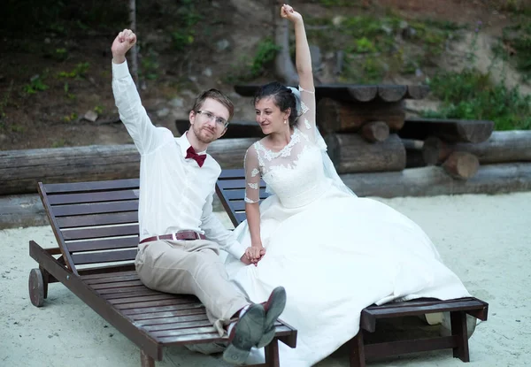 A noiva eo noivo nas espreguiçadeiras levantar as mãos para cima, celebrar o casamento e felicidade futura. — Fotografia de Stock