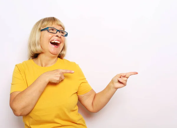 Retrato de alegre satisfeito satisfeito qualificado experiente alegre velha mulher apontando no vazio lugar em branco sobre ombro camisa amarela isolado no fundo cinza — Fotografia de Stock