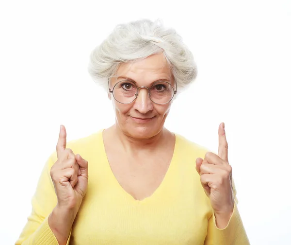 Portrait of a happy senior woman pointing upwards, isolated on a white background — Stock Photo, Image