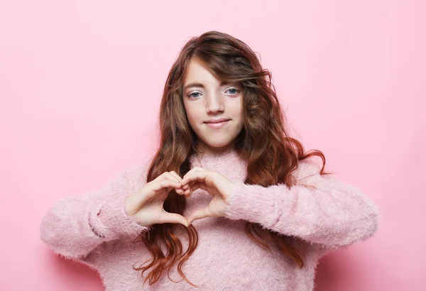 Positivo gentile bambina mostra il cuore fatto da mani alla macchina fotografica, ama tutti, isolato sfondo rosa — Foto Stock