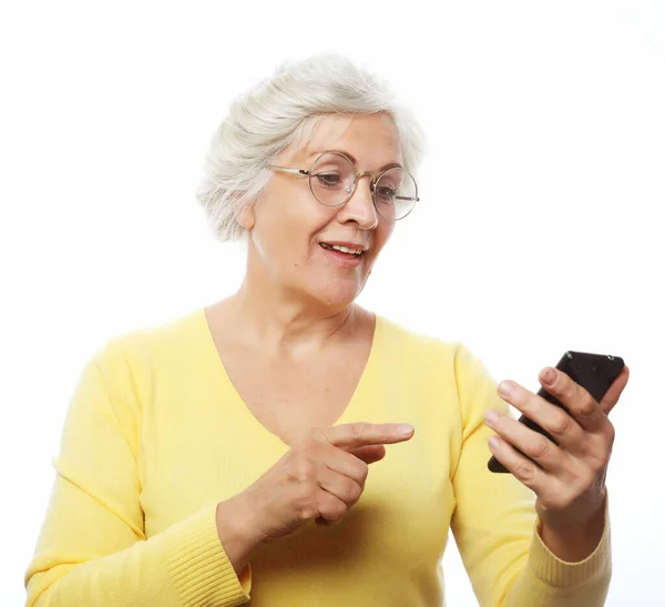 Όμορφη ηλικιωμένη γυναίκα με casual ντύσιμο χρησιμοποιώντας σύγχρονο smartphone και γελώντας δυνατά ενώ στέκεται σε λευκό φόντο. Γριά γυναίκα βλέποντας αστεία βίντεο στο διαδίκτυο. — Φωτογραφία Αρχείου