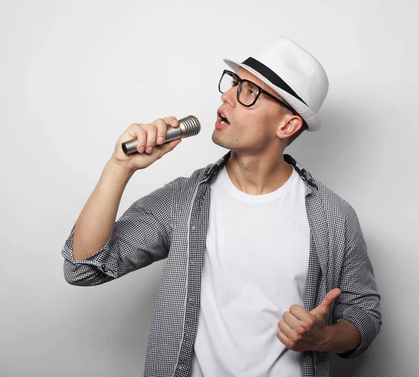 Lifestyle, people and leasure concept: ένας νεαρός άνδρας που φοράει γκρι πουκάμισο και καπέλο κρατώντας μικρόφωνο και τραγουδώντας. — Φωτογραφία Αρχείου