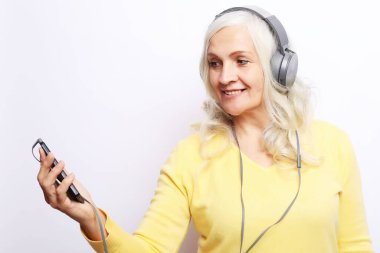 Neşeli yaşlı kadın, beyaz arka planda kulaklıkla müzik dinliyor.