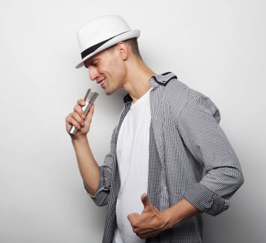 Yaşam tarzı, insanlar ve kiralık konsept: gri gömlekli ve şapkalı genç bir adam mikrofon tutuyor ve şarkı söylüyor..