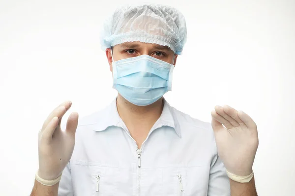 Un médico varón joven con máscara se coloca con las manos enguantadas, preparándose para un examen o cirugía del paciente —  Fotos de Stock