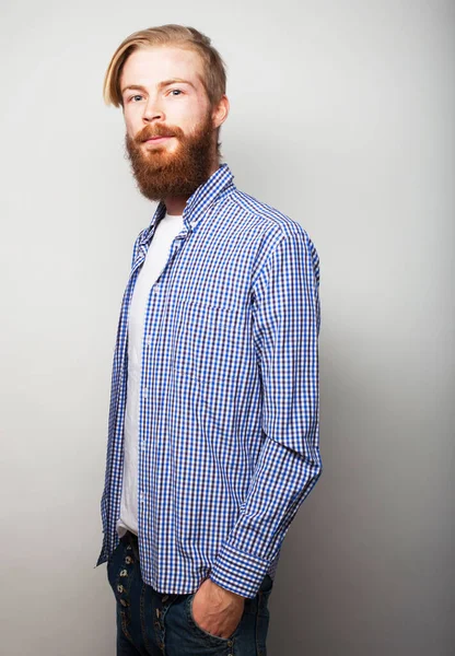 Красивый молодой бородатый мужчина в элегантной повседневной одежде смотрит в камеру, на сером фоне — стоковое фото