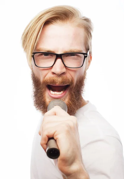 Mladý muž s vousy v bílé košili a brýlích, držící mikrofon a zpívající. — Stock fotografie